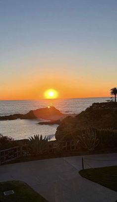 the sun is setting over the ocean with palm trees in the foreground and an island in the distance