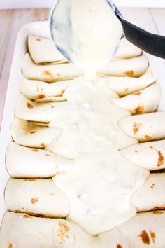 a pan filled with tortillas covered in white sauce and being drizzled