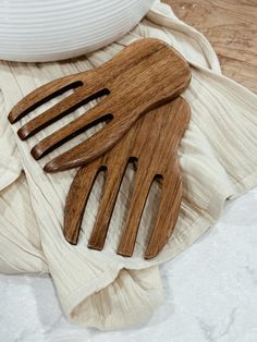 three wooden utensils sitting on top of a white cloth next to a bowl