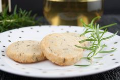 two cookies on a white plate next to a glass of wine and rosemary sprig