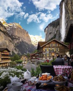 a table with food on it in front of a mountain range and waterfall, surrounded by mountains