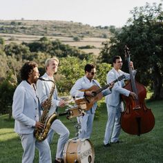 a group of men standing around each other with musical instruments in their hands and wearing white suits