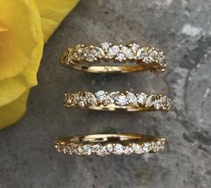 three different types of wedding rings sitting next to a yellow rose on a stone surface