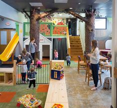 children are playing in an indoor play area with slides and climbing walls, while adults watch