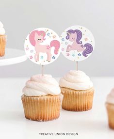 three cupcakes with pink frosting and unicorn toppers on white tablecloth