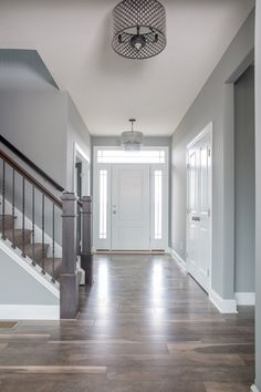 an empty hallway leading to a white door and some wooden stairs in a house with gray walls