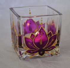 a glass vase with purple and gold designs on it's sides, sitting on a white surface