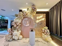 a table topped with balloons and flowers next to a wall covered in gold foil balls