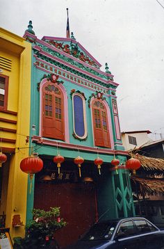 an old building with red and green trim on the front, next to a blue car