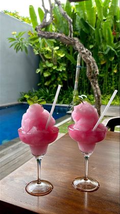 two glasses filled with ice cream sitting on top of a table next to a pool