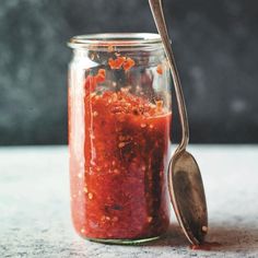 a jar filled with red sauce next to a spoon