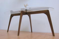 a table with a glass top and wooden legs on a hard wood flooring area