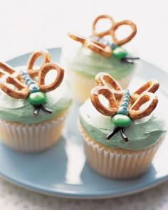 three cupcakes with green frosting and pretzels on top, sitting on a plate