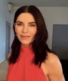 a woman in a red top is smiling at the camera and she has long dark hair