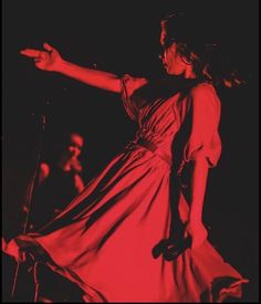 a woman in a red dress on stage with her arms out and one hand extended