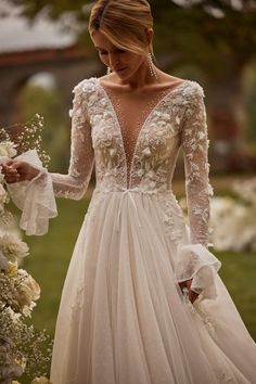 a woman in a wedding dress with flowers on the side and long sleeves, holding her bouquet