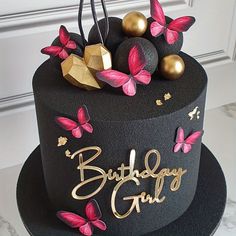 a black birthday cake with pink butterflies and gold decorations on it's top tier