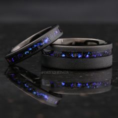 two wedding bands with blue and purple stars in them on a black surface, next to each other