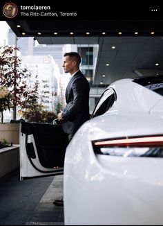 a man in a suit standing next to a white car