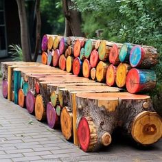 colorfully painted logs are lined up on the side of a brick sidewalk in front of some trees