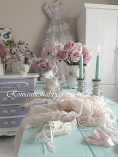 a blue table topped with lots of pink flowers next to white vases and candles