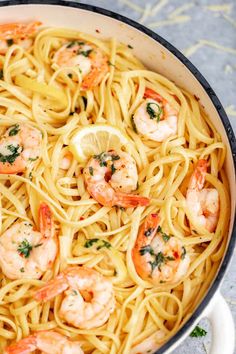 a pan filled with pasta and shrimp on top of a table next to lemon wedges