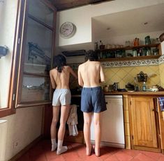 two people are standing in the kitchen looking out the window at the other person's back