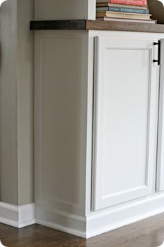 a bookshelf in the corner of a room with white cupboards and wood floors