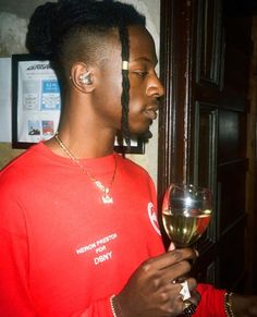 a man with dreadlocks holding a glass of wine in his hand and looking at it