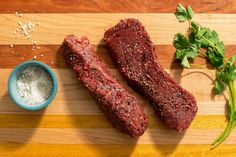 two raw meats on a cutting board next to some parsley and seasoning