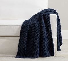 a blue crocheted blanket sitting on top of a white couch next to a white chair