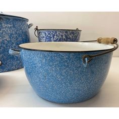 three blue pots with handles are sitting on a white counter top and one is empty