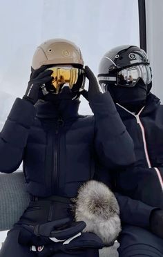 two people sitting on a bench wearing skis and holding their hats up to their faces