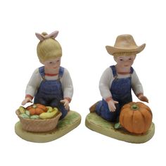 two figurines of children sitting next to each other with fruits and vegetables on them