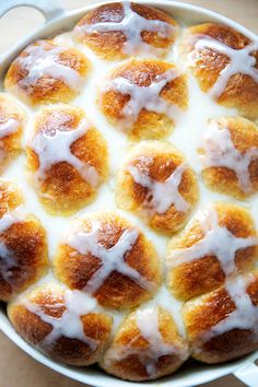 a pan filled with hot cross buns covered in white icing on top of a wooden table