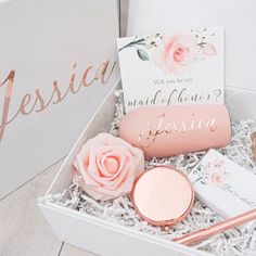 a box with some pink flowers and personal items in it on a wooden floor next to a sign