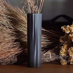 a black vase sitting on top of a wooden table next to dried plants and a teddy bear