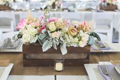 a wooden box filled with lots of flowers on top of a white table cloth covered table