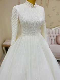 a white wedding dress with long sleeves and beadings on the skirt is displayed in front of a couch