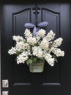 a black front door with white flowers in a bucket