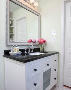 a bathroom vanity with black counter top and white cabinets, pink flowers on the mirror