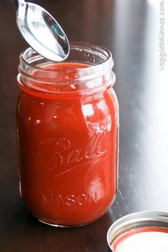 a jar filled with red sauce sitting on top of a table next to a spoon