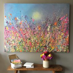 a painting is on the wall next to a table with books and flowers in it