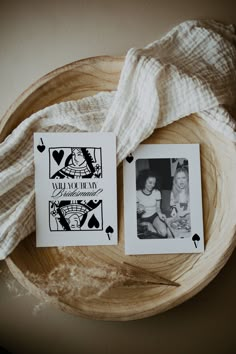 two cards that have been placed on a wooden plate next to a white cloth and some black and white photos