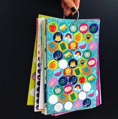 a hand holding an open notebook with stickers on it and several different colored papers