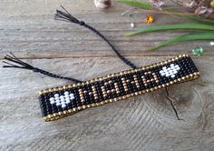 a beaded bracelet sitting on top of a wooden table next to flowers and greenery