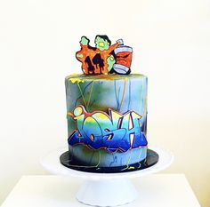 a multi - colored cake with graffiti on it sitting on a white pedestal in front of a wall