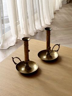 two metal candlesticks sitting on top of a wooden table next to a window