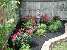 a garden area with flowers and a statue in the center, along side a fence