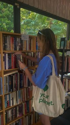 a woman is looking at books in a book store while holding a tote bag